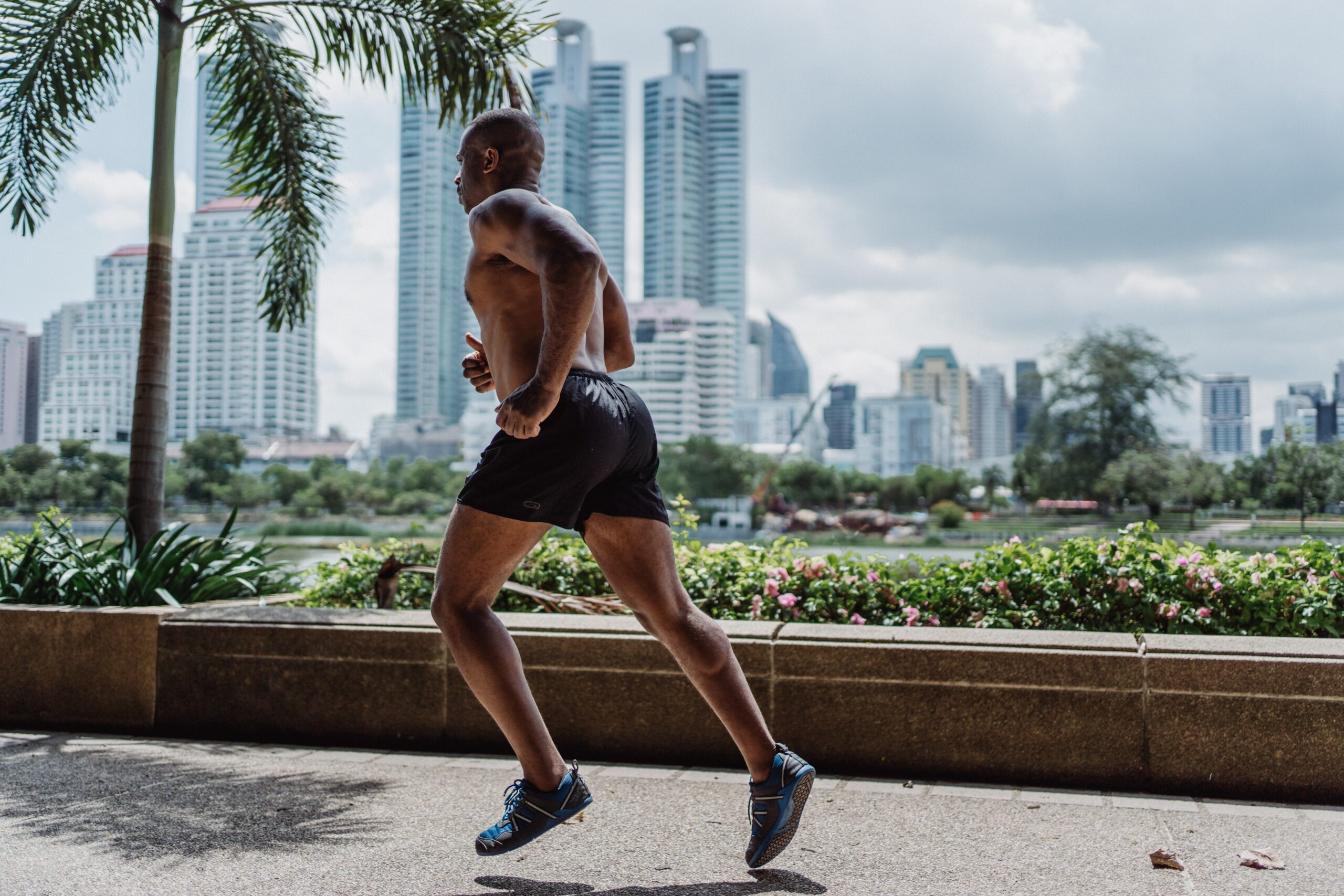 A black male jogging outdoors, wearing athletic attire and displaying determination and focus in his stride.